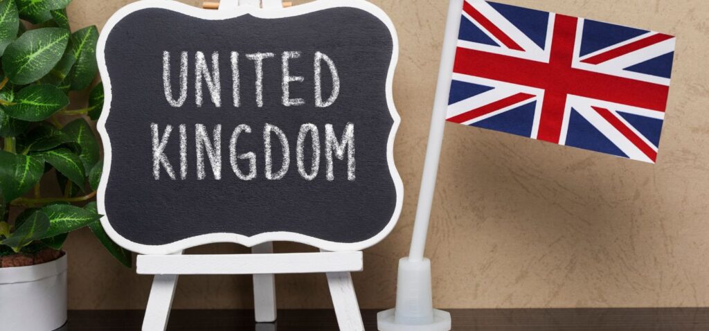 A mini chalkboard on an easel with "UNITED KINGDOM" written on it in white chalk is displayed beside a small tabletop flag of the United Kingdom.